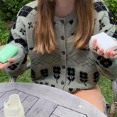 Person wearing a patterned cardigan holding soap bars outdoors
